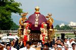 御霊さんで一初を　大田ノ沢で杜若 : 渡月橋を背景に剣鉾、神輿が練る